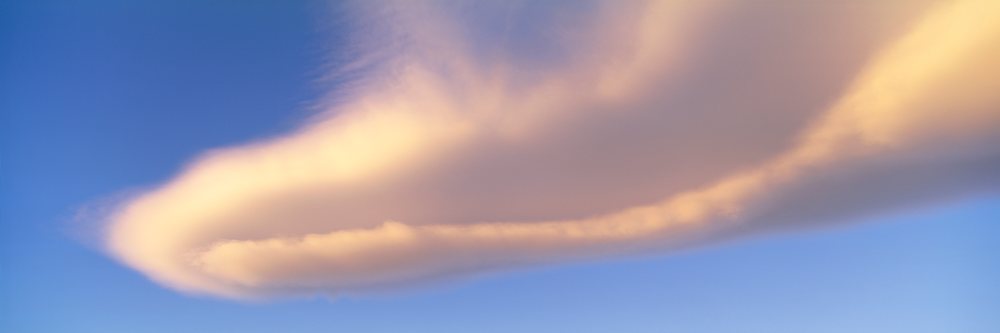 Clouds illuminated by sunlight against a clear blue sky at sunset.