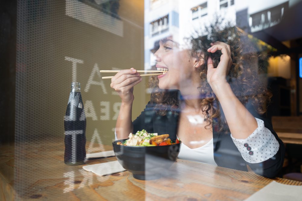 Businesswoman eating lunch with chopsticks from a bowl of healthy food inside a restaurant, traveling executive, Spain.