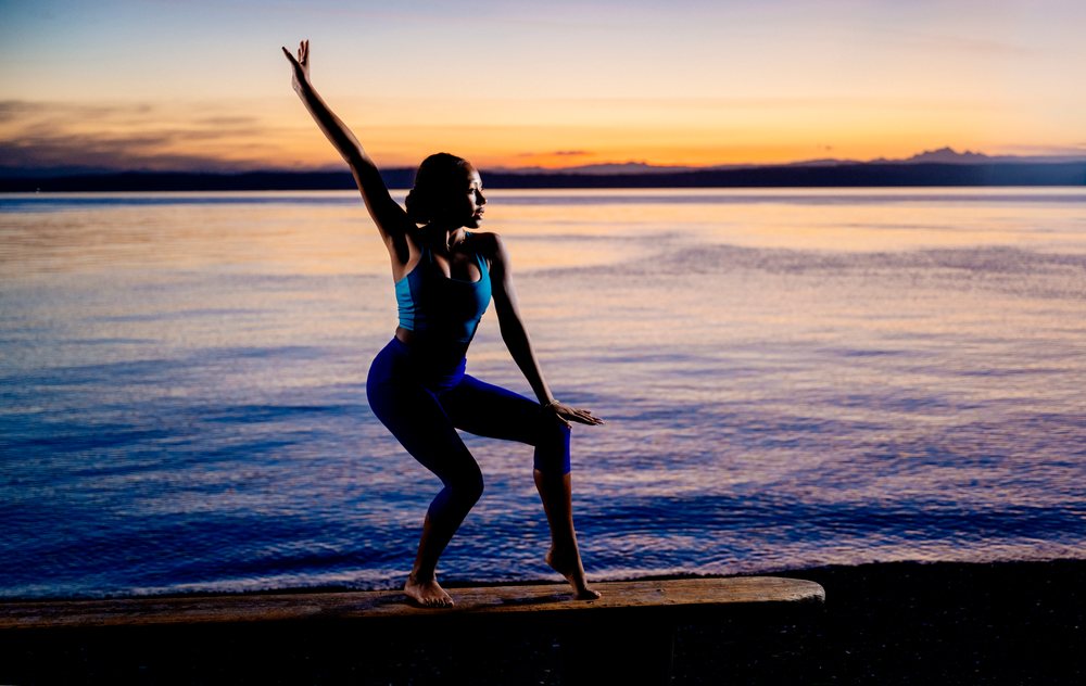 Woman balancing barefoot on a wooden bench practicing yoga and acrobatics at ocean sunset, USA.
