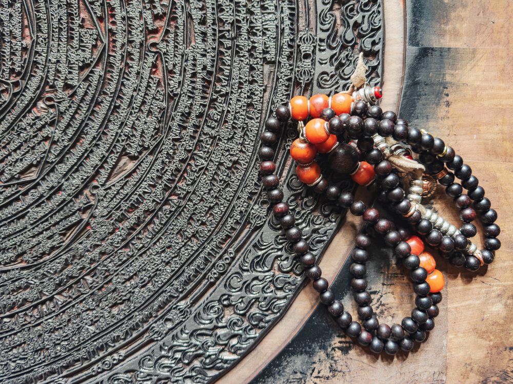 Intricately carved Corcular Printing Block with Tibetan script and dark brown and red prayer beads resting on a wooden surface at Dege Printing Monastery, Sichuan Province, People's Republic of China.