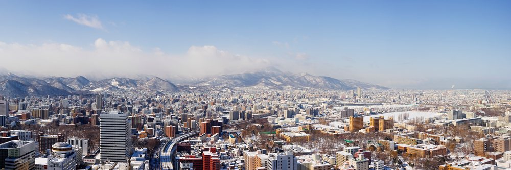 Snow-covered city skyline and mountain range under a blue sky in Sapporo during winter, Hokkaido, Japan.