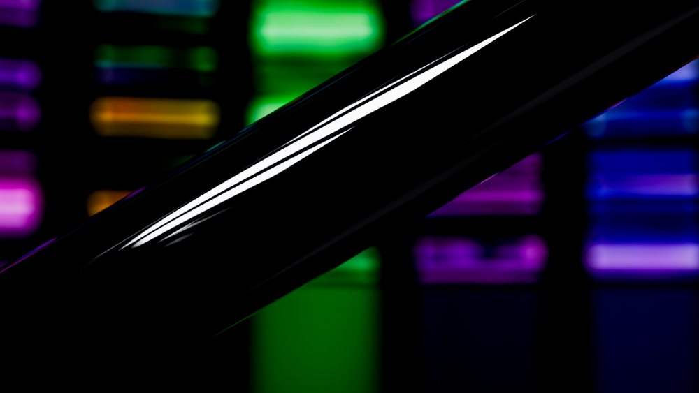 Close-up of a black glass test tube reflecting colorful lights in a laboratory setting with blurred light panels in the background.