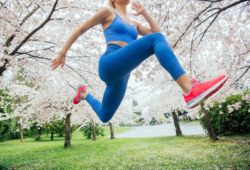 Woman jumping outdoors in a park with cherry blossom trees during spring, USA.