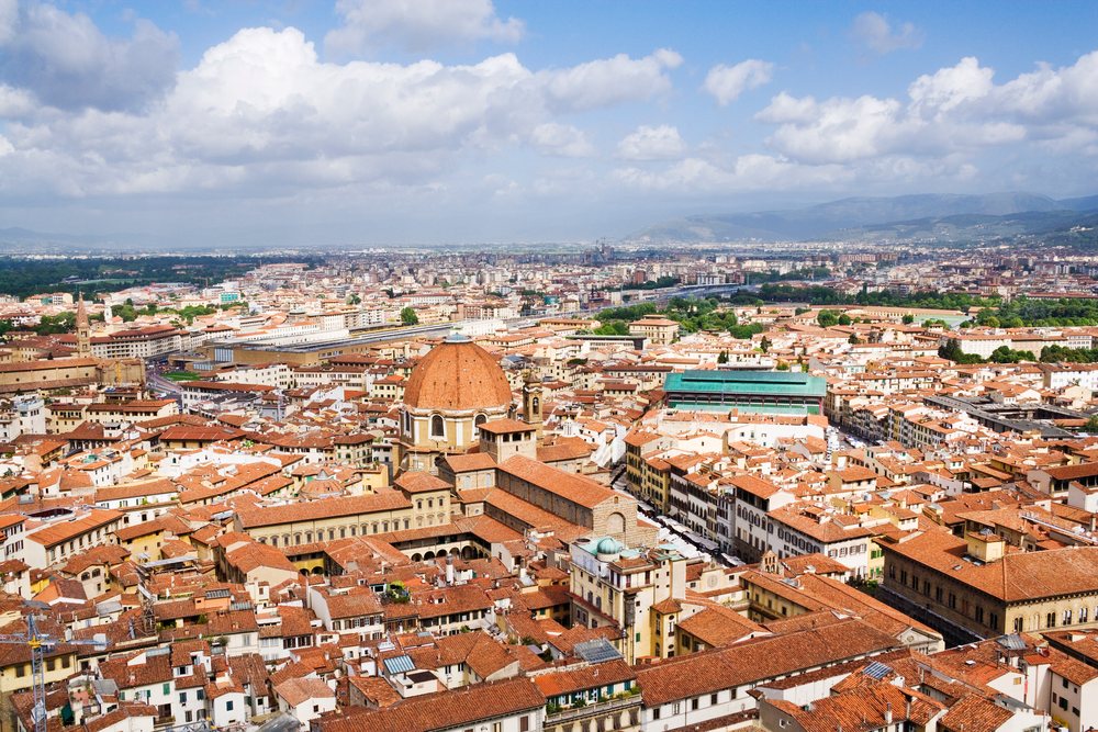 View from Duomo looking towards Basilica di San Lorenzo over Florence's cityscape with historic red tile roofs and distant mountains, Italy.