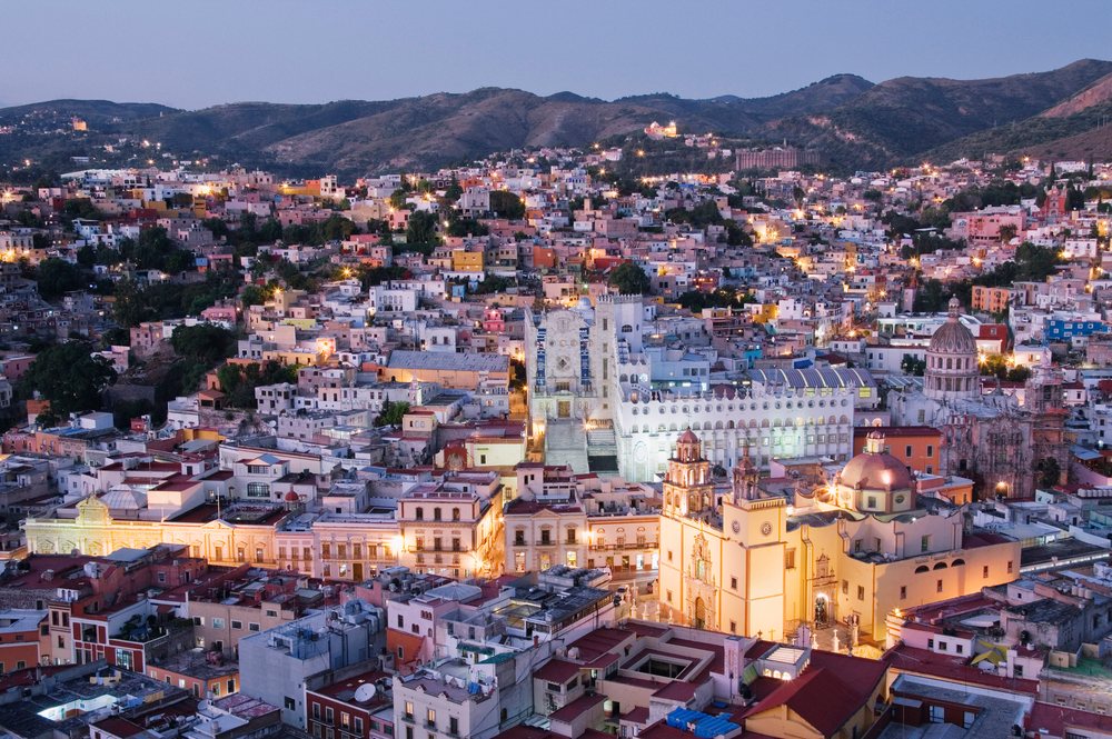 Guanajuato cityscape at twilight showing illuminated buildings with hills behind the urban area.