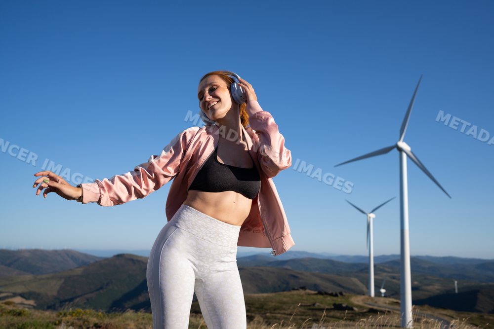 Young white woman dancing near wind turbines in Galicia, Spain