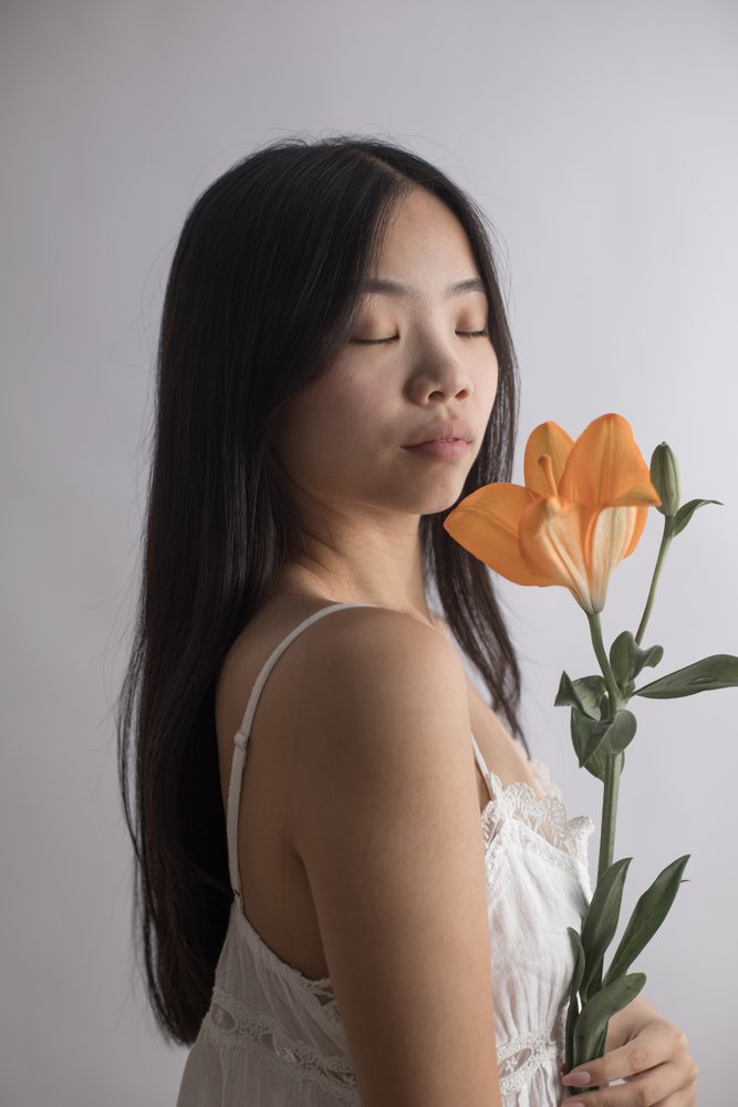 Woman holding an orange lily with a flower bud and stem in a serene studio portrait with closed eyes and a calm expression, Art, emotional.