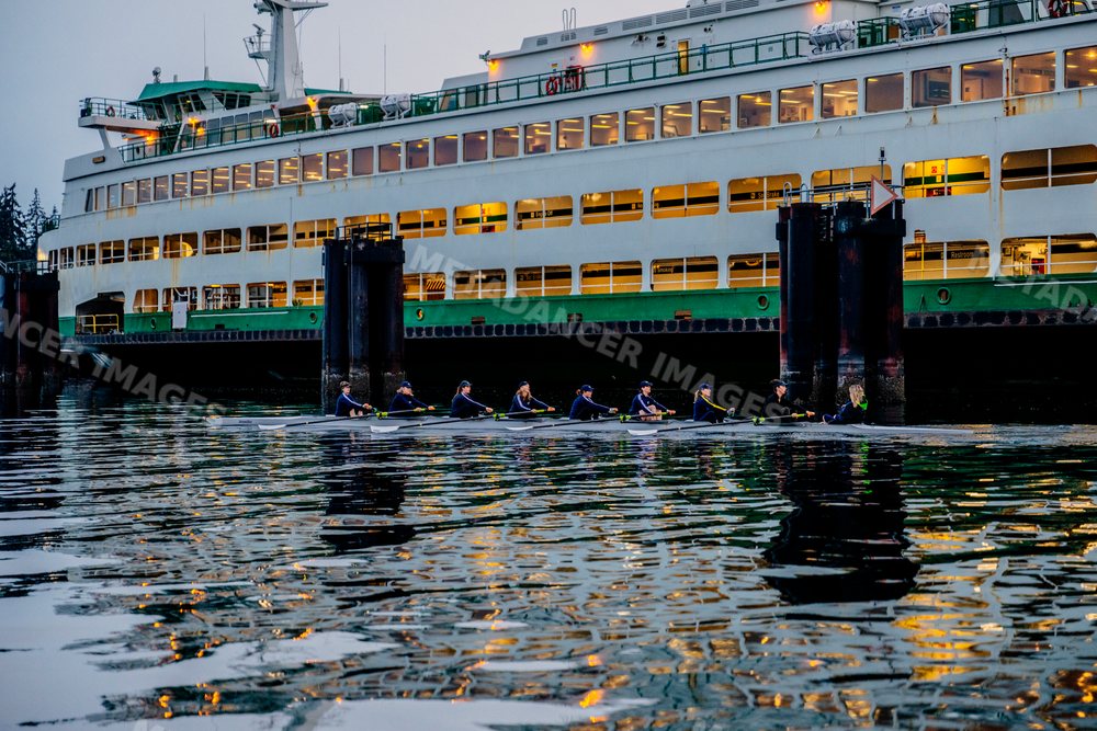A rowing team practicing on calm water near a ferry dock in wa USA