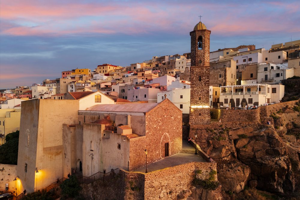 Cattedrale di Sant'Antonio Abate church and bell tower at Dusk overlook clustered hillside houses and rocky cliff, Travel Images, Castelsardo, Sardinia, Italy.