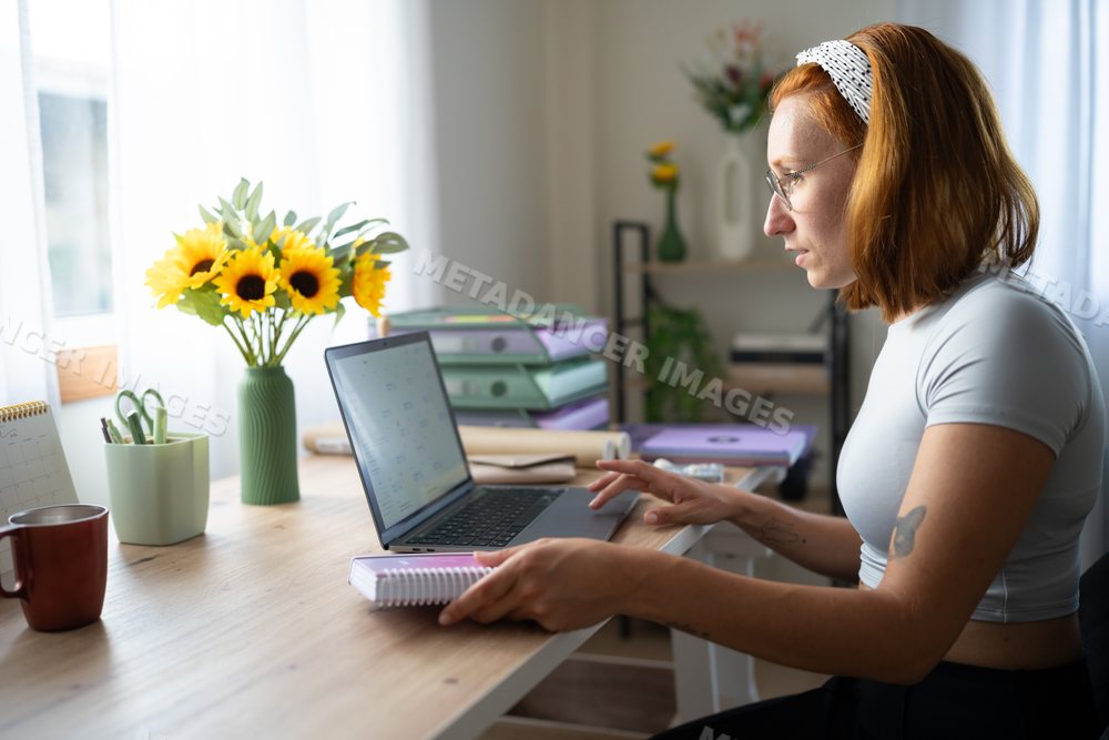 A white woman works on a laptop at a neat home office desk