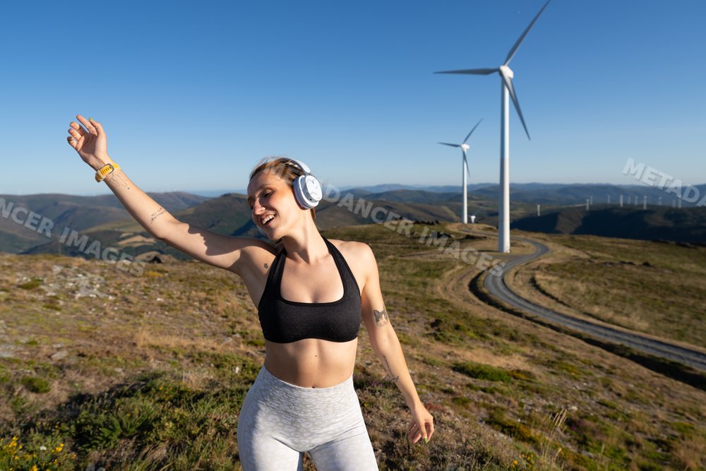 Young white woman dances happily near wind turbines in Galicia, Spain