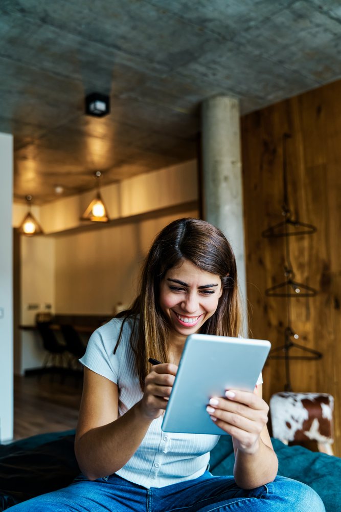 A woman happily uses a tablet with a stylus