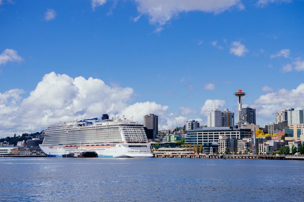 Cruise ship docked at Seattle waterfront with Space Needle and city skyline under blue sky and white clouds, USA.