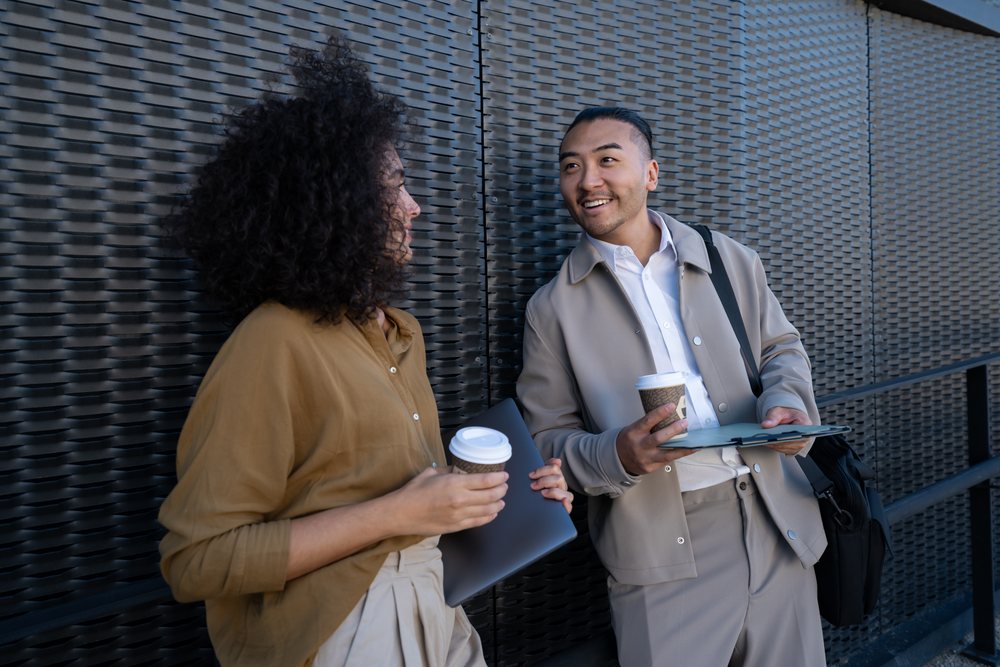 Two people holding coffee cups and working with a laptop and clipboard outdoors in an urban setting, Madrid, Spain.