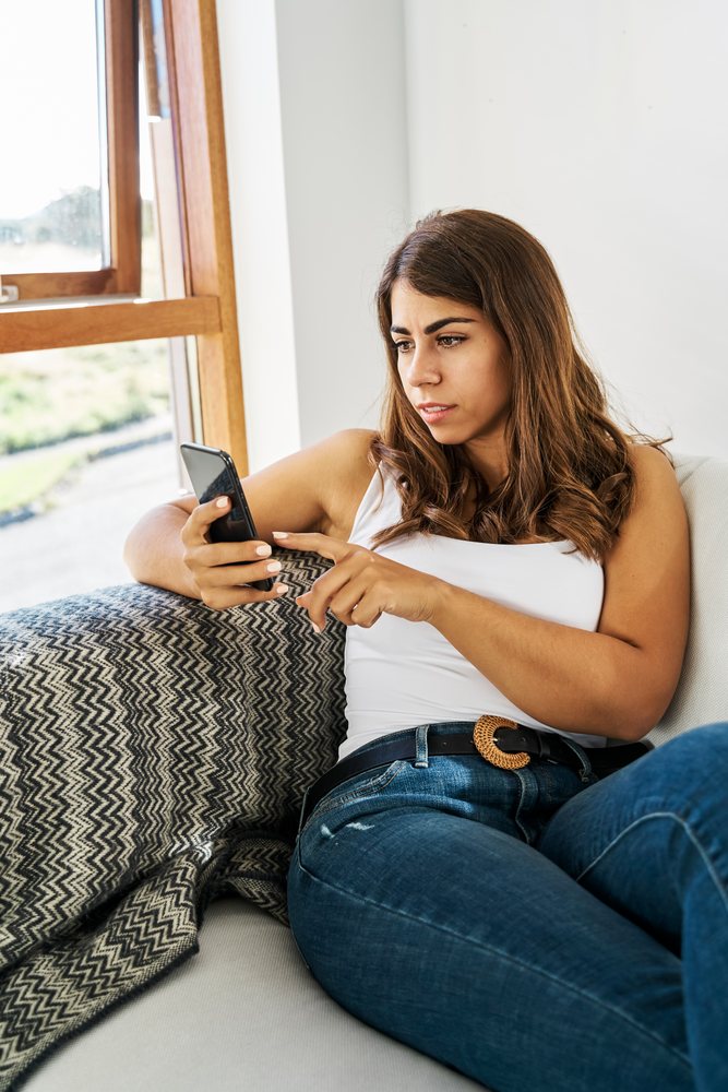 A white woman sitting on a couch using her smartphone indoors