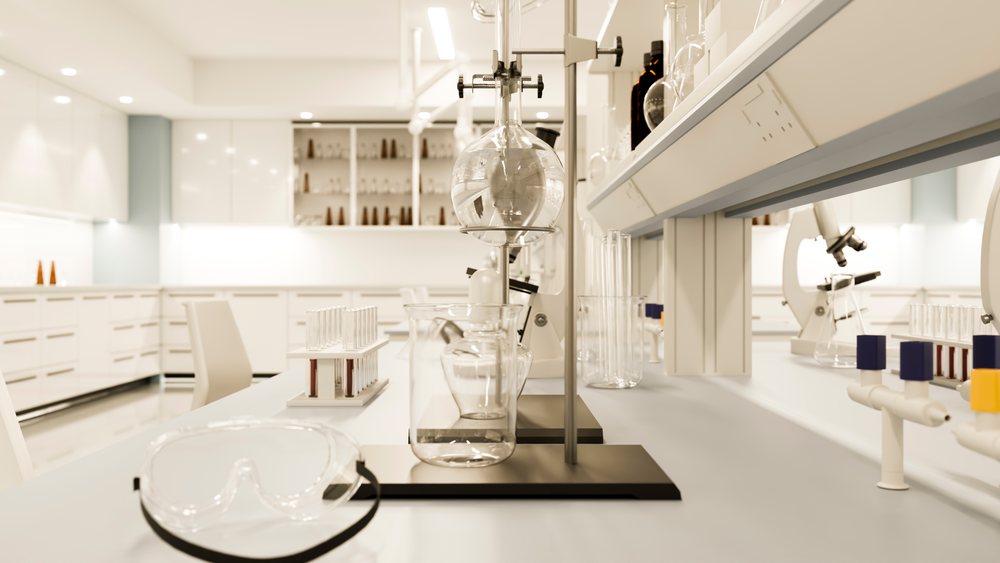 Scientific laboratory with chemical glassware, microscopes, and lab goggles arranged on a clean lab bench in a modern research setting.