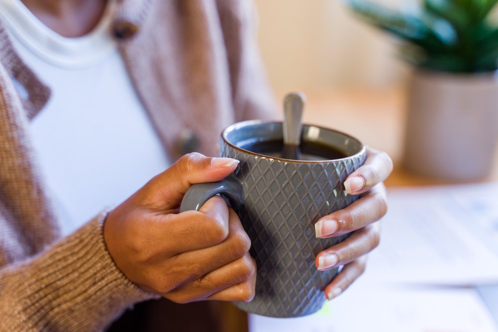 Person holding a textured ceramic mug filled with hot coffee with a spoon, seated indoors at a table, Spain.