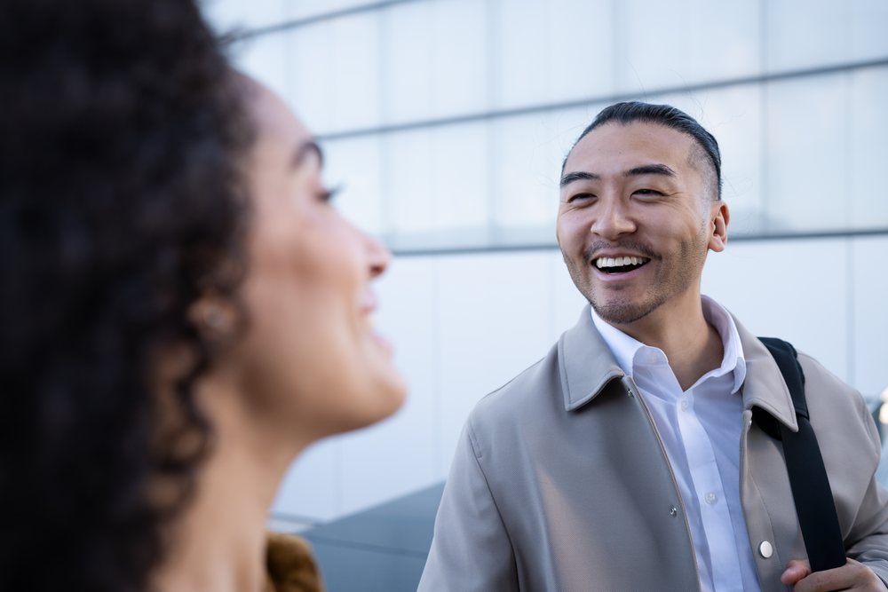Man smiling and talking with woman outdoors against a modern urban wall, Madrid, Spain.