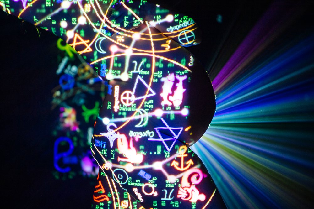 Silhouette of a pregnant woman with colorful projected symbols and light rays on a black background, pregnancy.