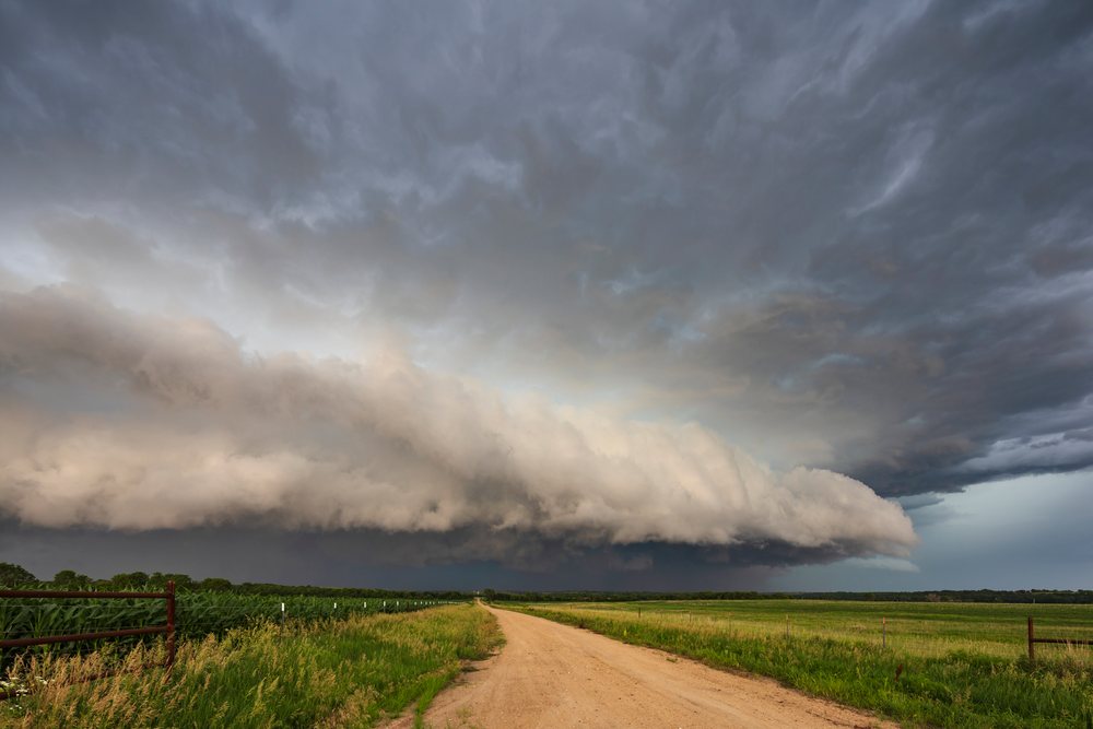 Supercell storm clouds gather over a rural dirt road and fields, in Tornado Alley, Weather, Environmental Issues, Storm Chasing, Waterville, Kansas, USA.