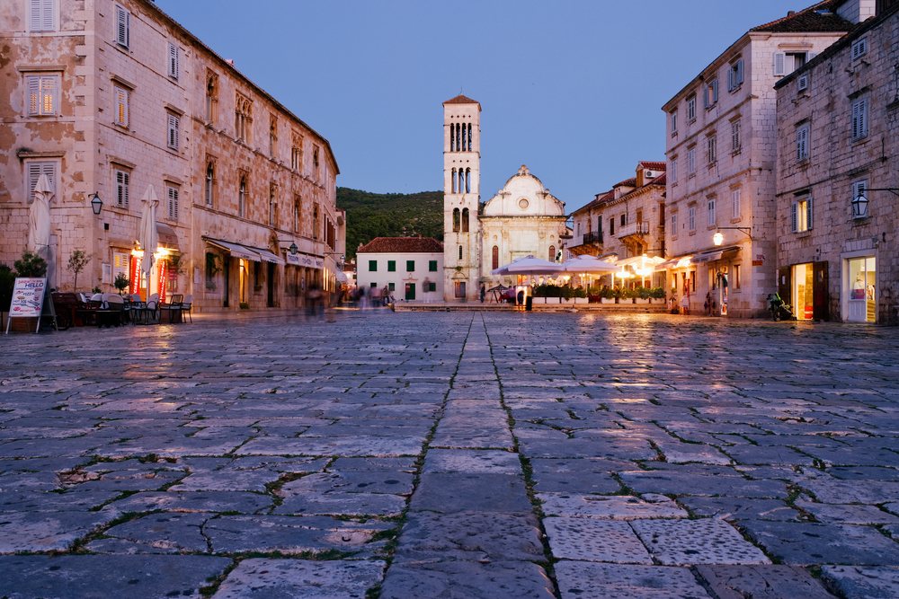 Stone paved square with a church tower and historic buildings at evening twilight, Hvar, Croatia.
