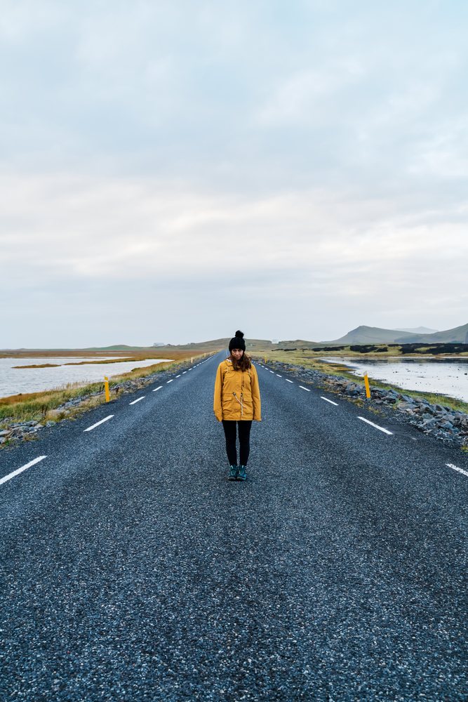 A white woman stands alone on a paved road