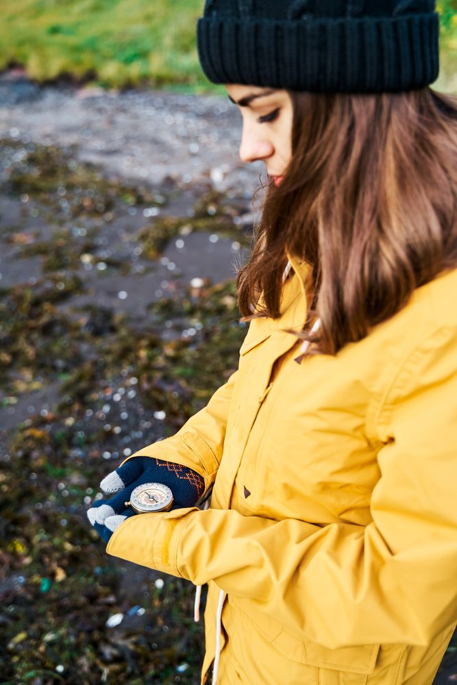 A white woman examines a compass while standing outdoors
