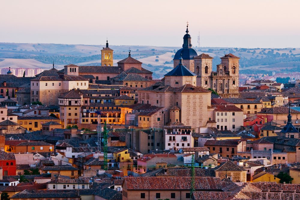 Cityscape of historic Toledo with church towers and rooftops at evening twilight under a clear sky, Spain.