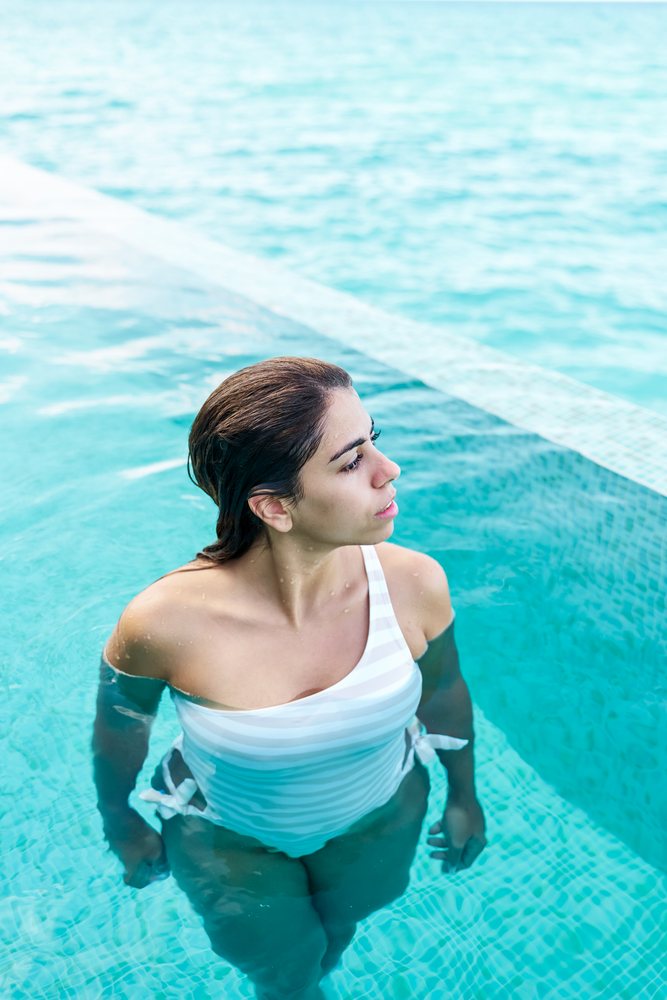 A white woman relaxes in a turquoise tiled swimming pool