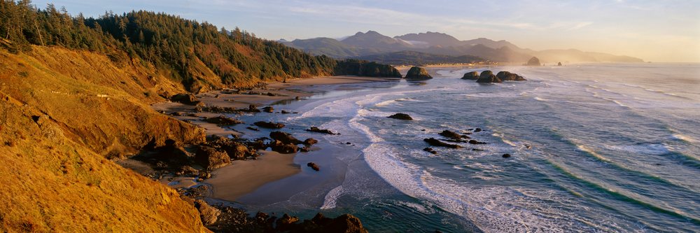 Panoramic view of Ecola State Park coastline with waves, rocky formations, and forested cliffs at sunset in Oregon, Ecola State Park Oregon, USA.