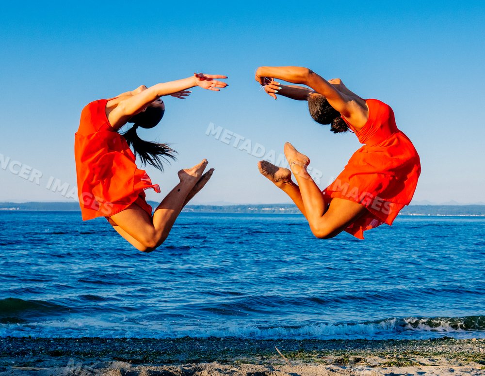Two women in red dresses perform synchronized jumps at the beach