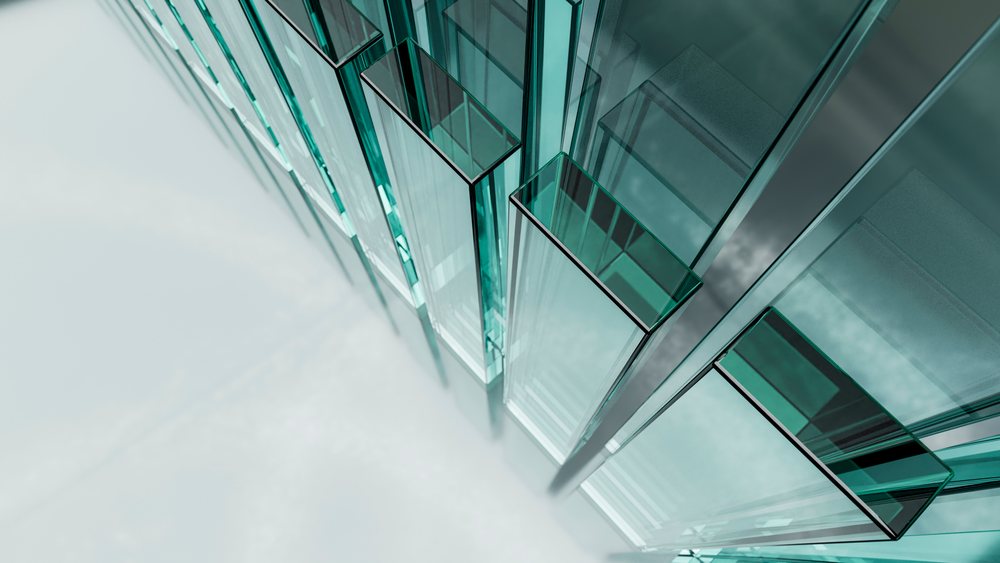 Vertical transparent glass panes with blue tint and steel framing form a modern architectural structure with reflective surfaces in an urban setting.