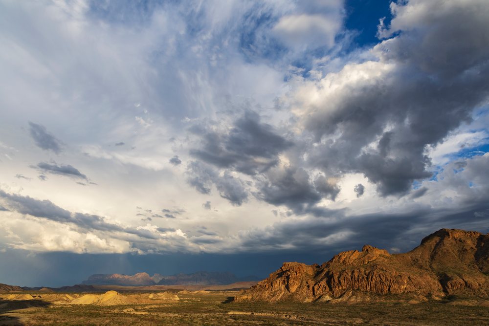 Stormy skies cast dramatic light over the rugged Chisos Mountains and desert landscape, Study Butte, Texas, USA.