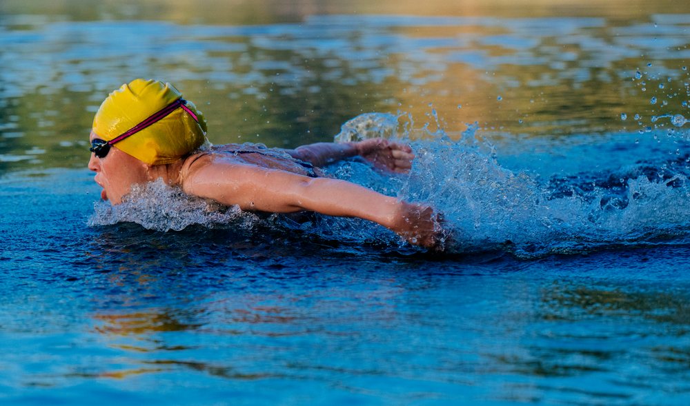Swimmer performing butterfly stroke in open water wearing a yellow swim cap and goggles, USA.