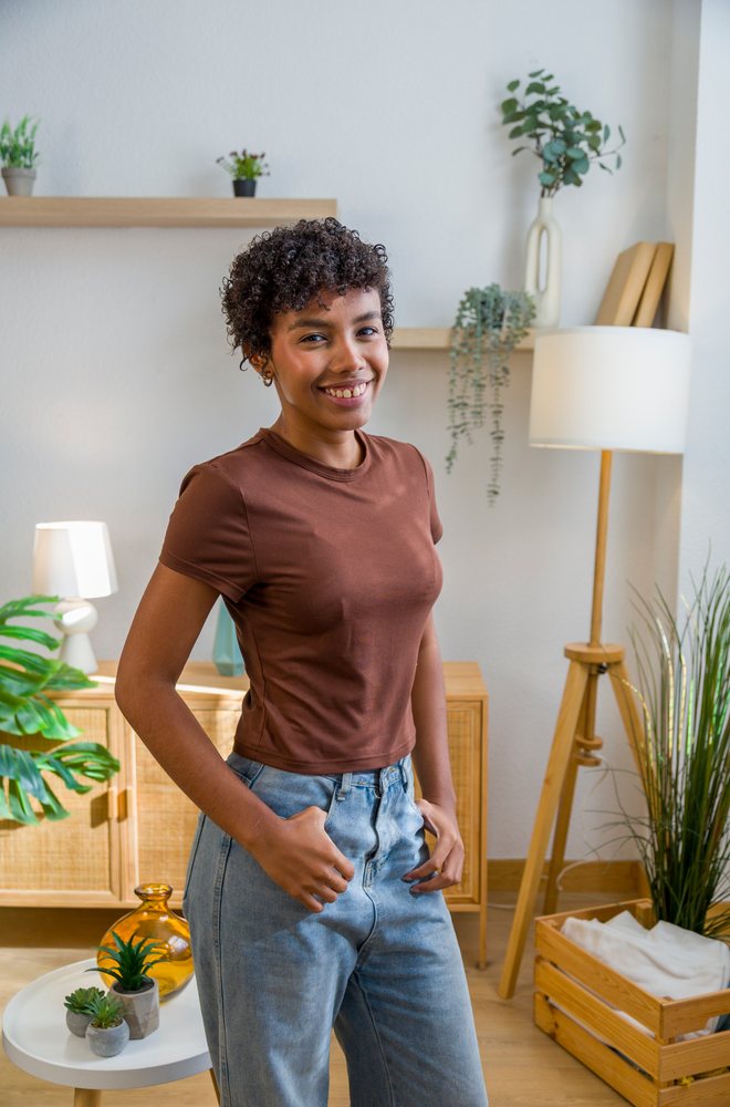 Woman smiling and standing indoors in a modern home environment with wood furniture and potted plants.