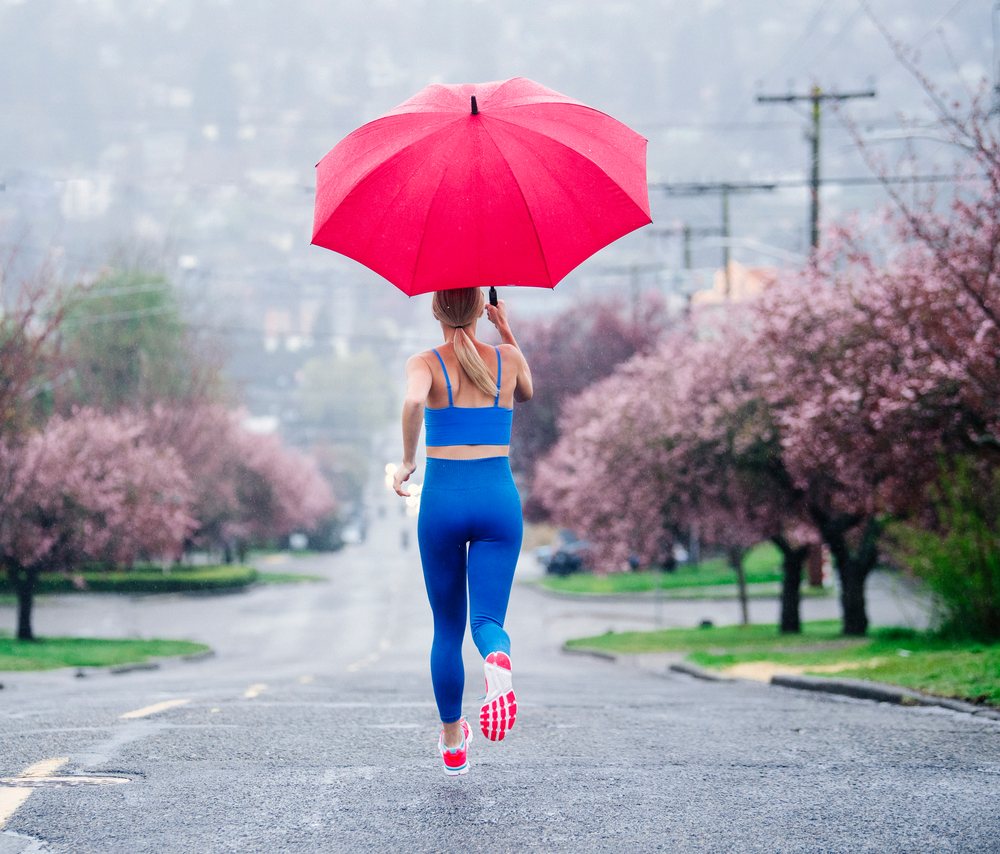 Woman runs on a rainy street lined with blossoming pink trees holding a red umbrella, USA.