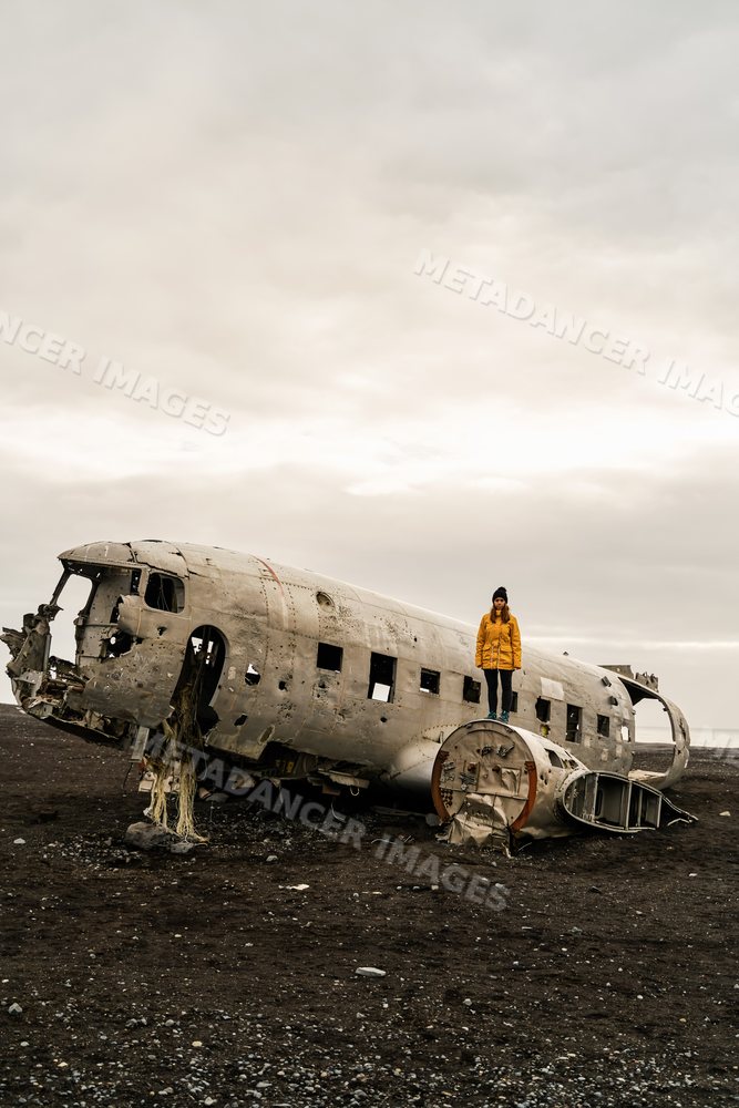 A white woman stands on an abandoned crashed airplane fuselage