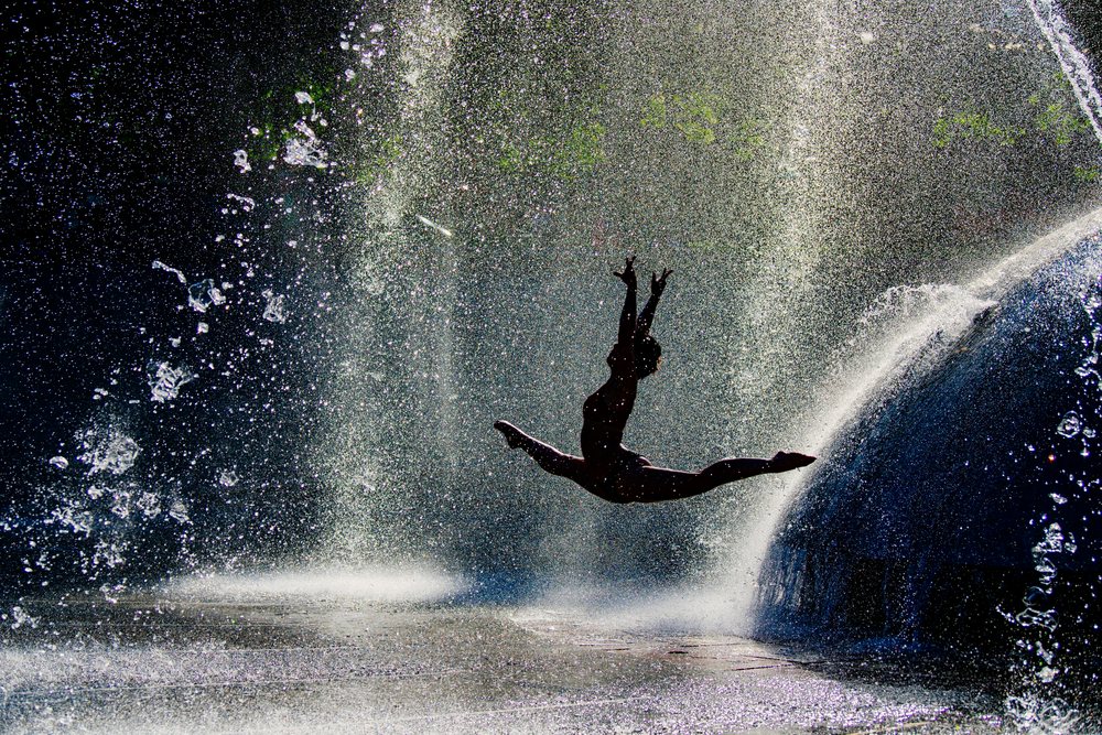 Silhouette of a female dancer leaping through a water fountain outdoors in bright light, USA.