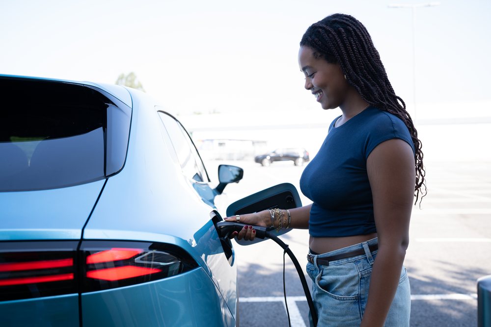 A woman is charging an electric vehicle with a charging cable in an outdoor parking lot, green energy, sustainability, mobility, Spain, Europe.