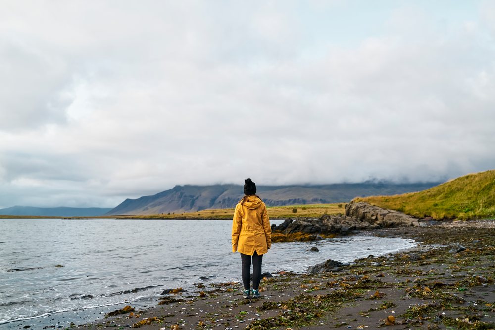 A white woman stands on a rocky shore looking