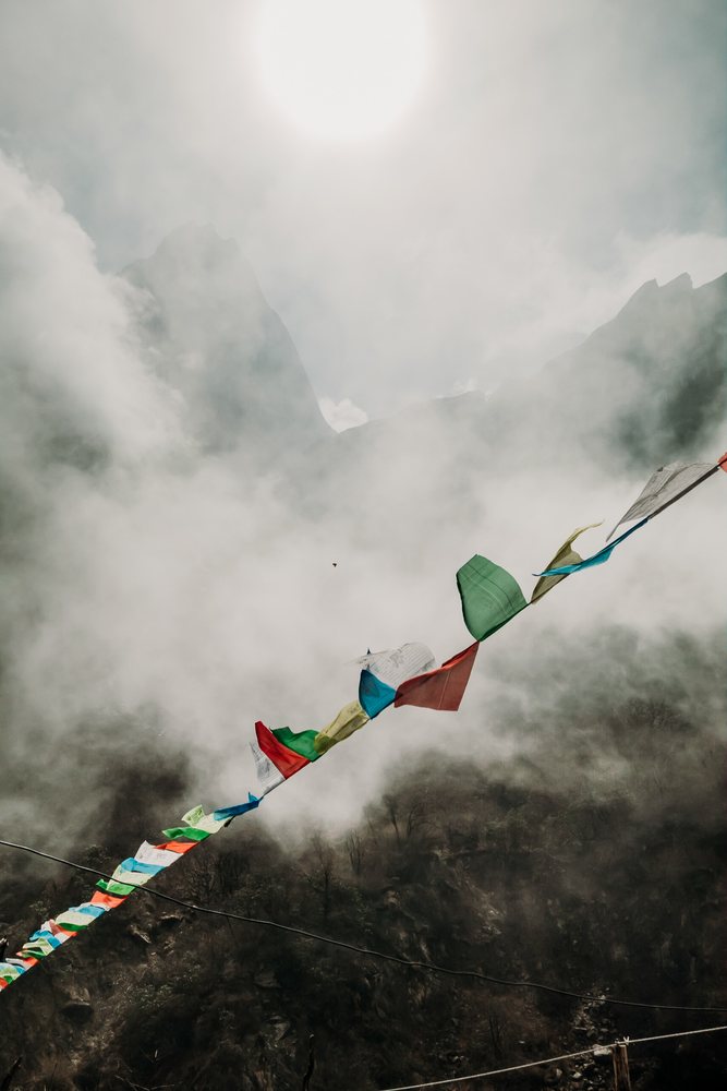 Prayer flags flutter over misty rocky mountains under the sun in a mountaineering landscape, Nepal.