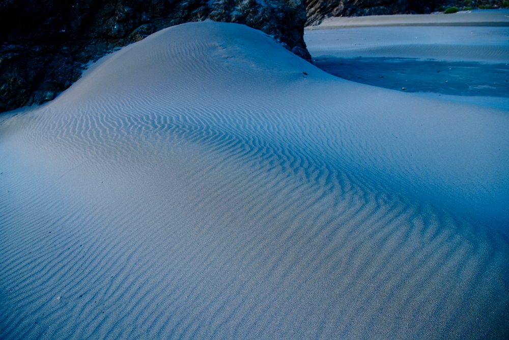 Sand dune with ripple patterns beside a coastal rock formation on a beach shoreline, Meyers Creek, Oregon, USA.