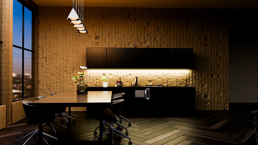 Modern kitchen workspace features wooden table with flower vase, black cabinetry, pendant lights, and brick wall at night.