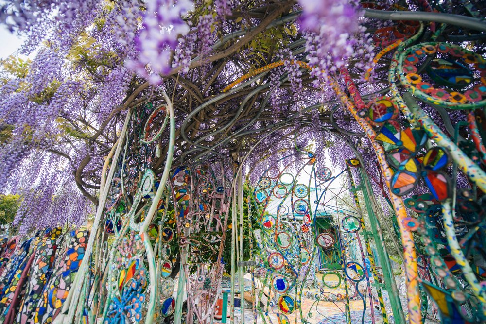 Purple flowering wisteria vine growing over a decorative colorful mosaic metal arch in an outdoor garden, CA, USA.