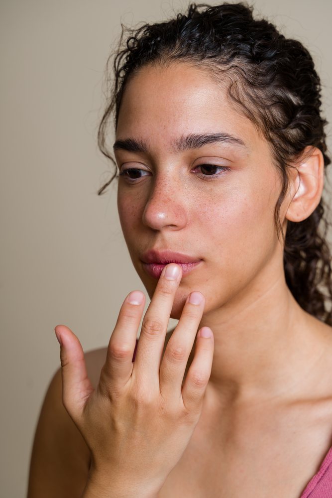 Close-up portrait of a woman with curly hair touching her lips in an indoor setting, beauty shoot, Spain.