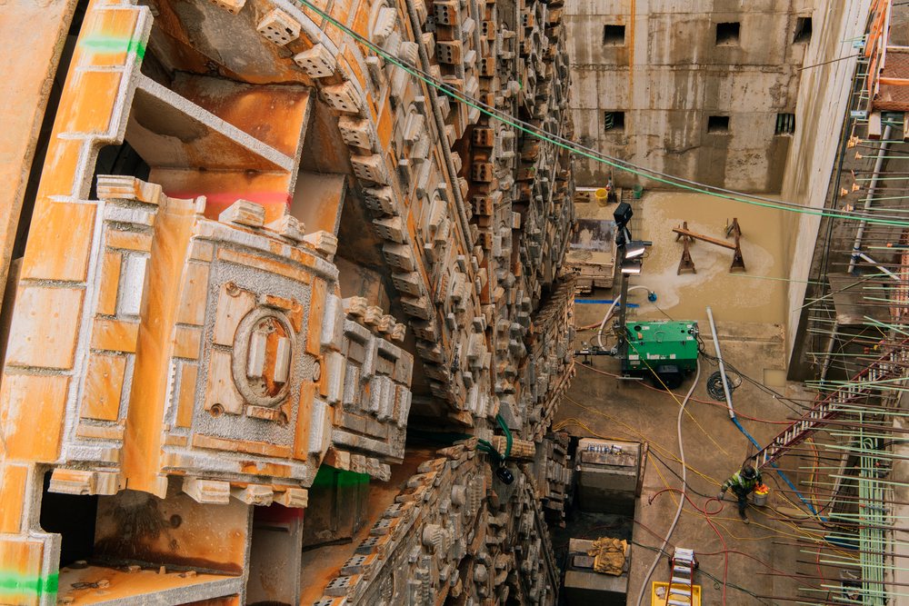 A large tunnel boring machine is operating at a construction excavation site in the USA, surrounded by construction equipment and workers, a large tunnel boring machine, tunnel, drilling.