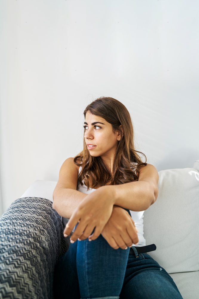 A young white woman sitting thoughtfully on a sofa