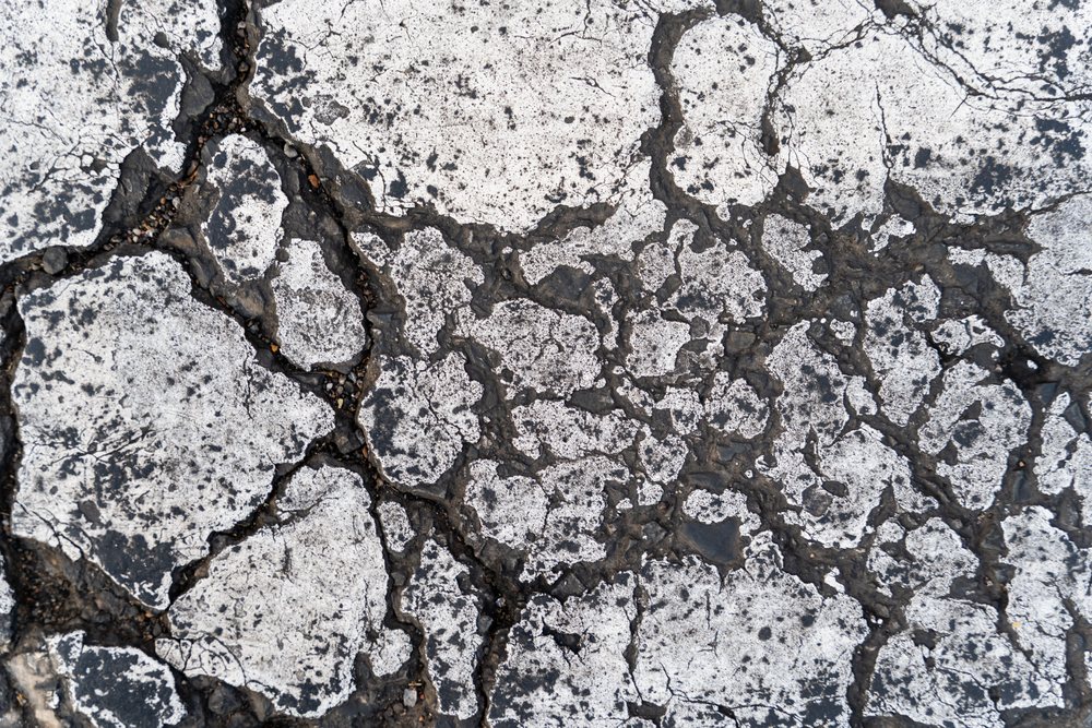 Black and white photo of cracked and weathered asphalt pavement with rough texture outdoors, abstract texture, background, wallpaper, Spain.