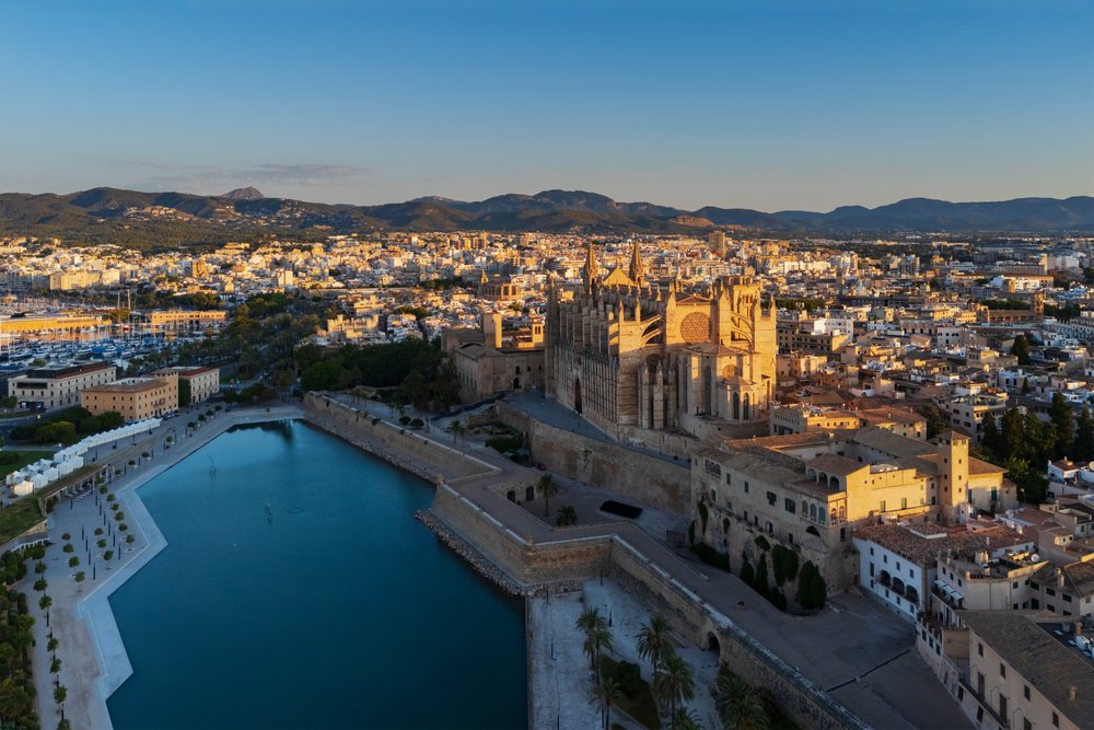 Cathedral in Palma de Mallorca overlooks harbor, city buildings, and distant mountains at sunset, Landscape, Lifestyle, Balearic Islands, Spain.