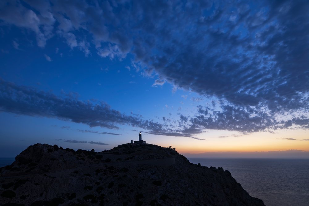 Far de Formentor Lighthouse illuminated on a rocky cliff at sunrise with ocean and cloudy sky, Landscape, Lifestyle, Pollença, Mallorca, Spain.